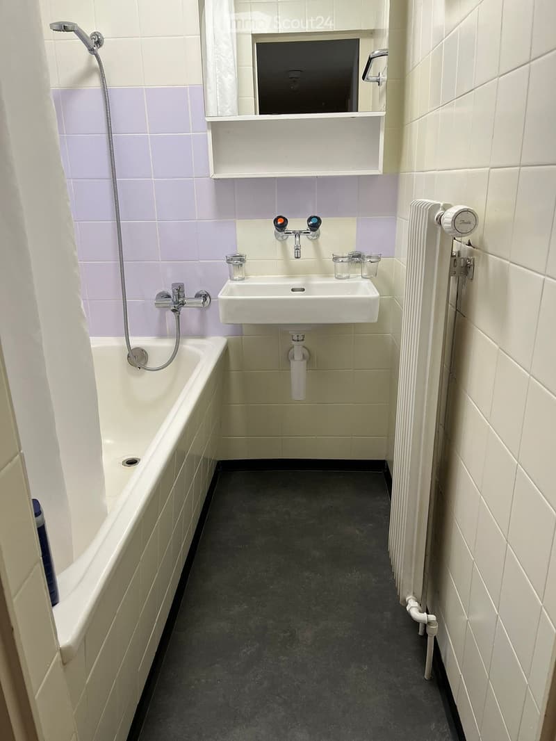 Bathroom with a bathtub, sink, faucet, radiator, mirror, and cups on the sink.