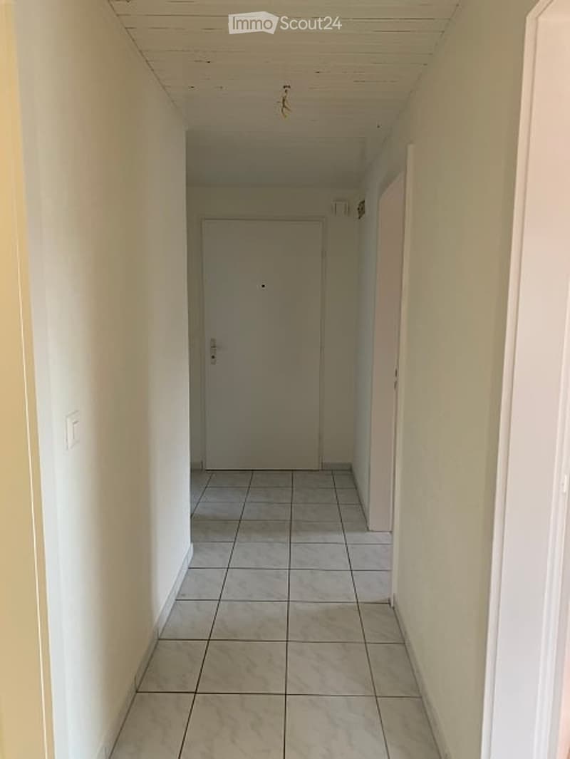 Empty hallway with tiled floor, white walls, and a closed door at the end.