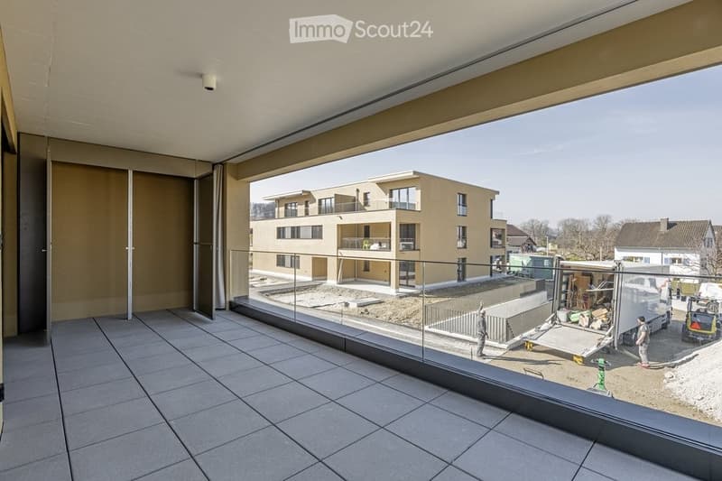 Spacious balcony with large glass sliding doors, tiled floor, and a view of a modern residential building under construction.