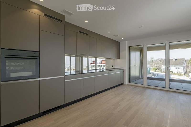 Modern kitchen with grey cabinets, wooden flooring, large windows, and a view of the outdoor area.