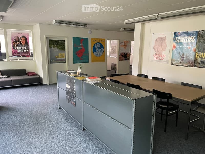 Office space with a reception desk, sofa, table with chairs, and several posters on the walls.
