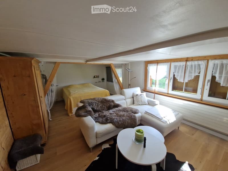 Bright, open living space with a white sectional sofa, a small round coffee table, a bed with a yellow cover, and large windows with white curtains.