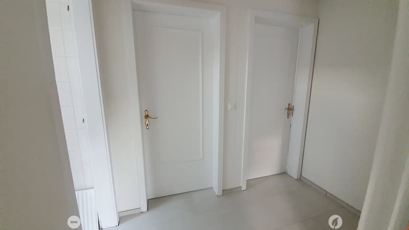 Empty hallway with white tiled floor and two white doors with gold handles.