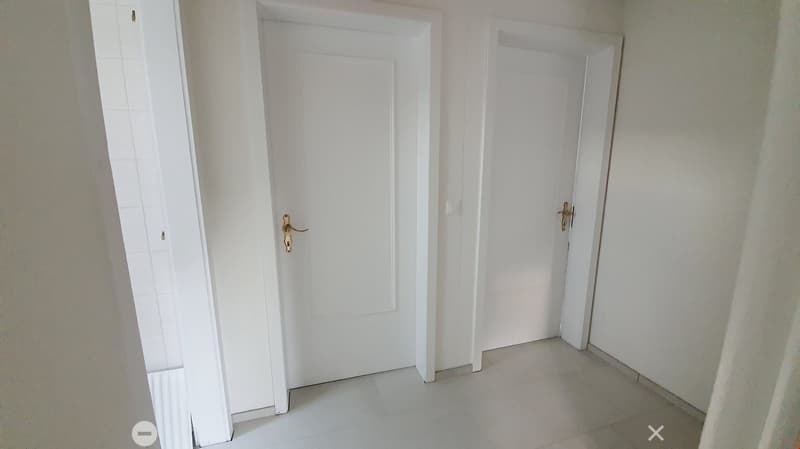 Empty hallway with white tiled floor and two white doors with gold handles.
