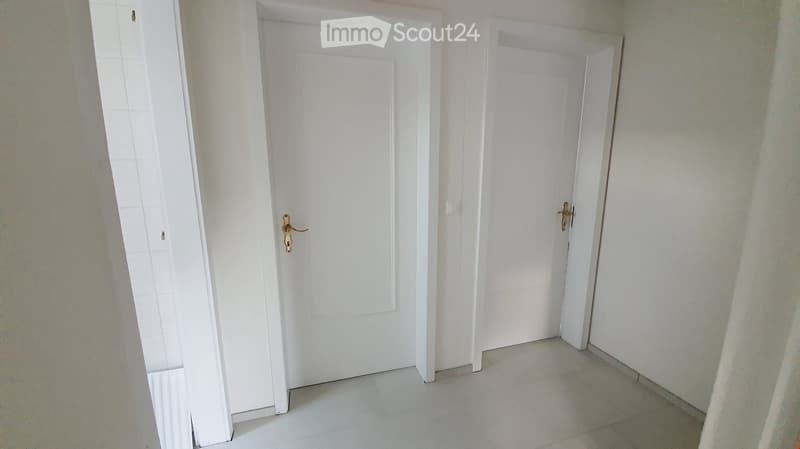 Empty hallway with white tiled floor and two white doors with gold handles.