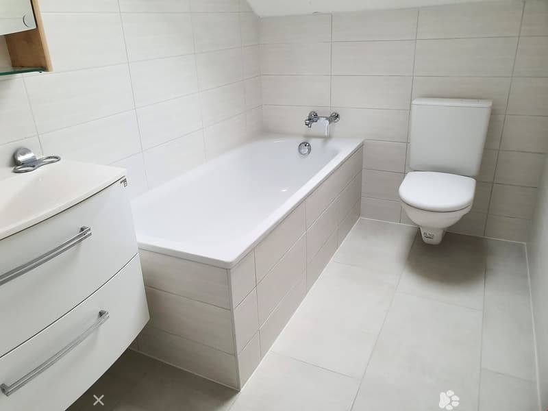 Modern bathroom with white tiles, a bathtub, a toilet, a sink with a cabinet, and a glass shelf above the sink.