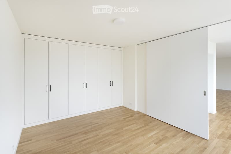 Completely empty room with white walls, light wooden flooring, and built-in white wardrobes.