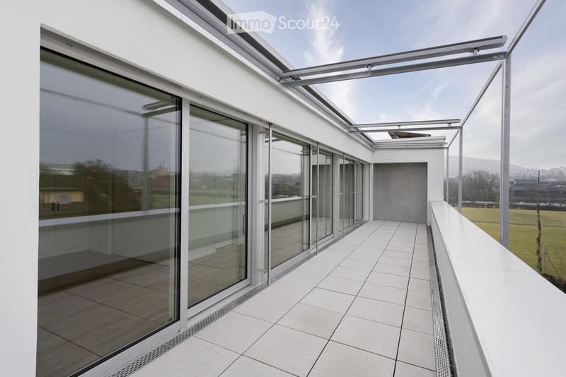 Modern rooftop terrace with large glass sliding doors, white tiled flooring, and a retractable roof system. Offers panoramic city views.