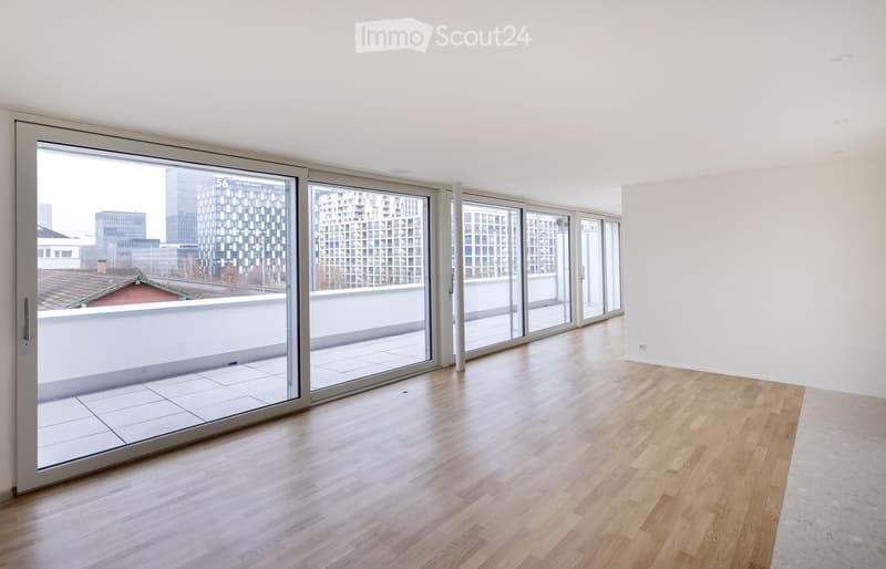 Empty room with wooden flooring, large sliding glass doors leading to a balcony, and a view of city buildings.