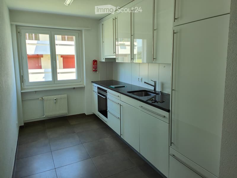 Modern kitchen with white cabinets, dark countertops, a sink, and an oven. The space features tiled flooring and a window with blinds.