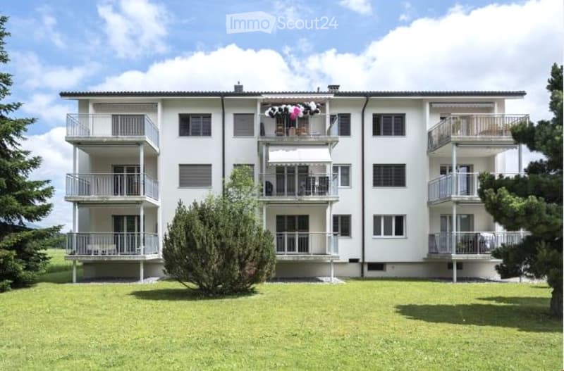 Multi-story residential building with multiple balconies and a well-maintained lawn in front.