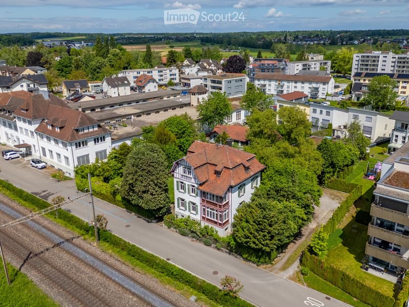 Aerial view of a residential area with multiple houses, trees, and a train track running through the scene.