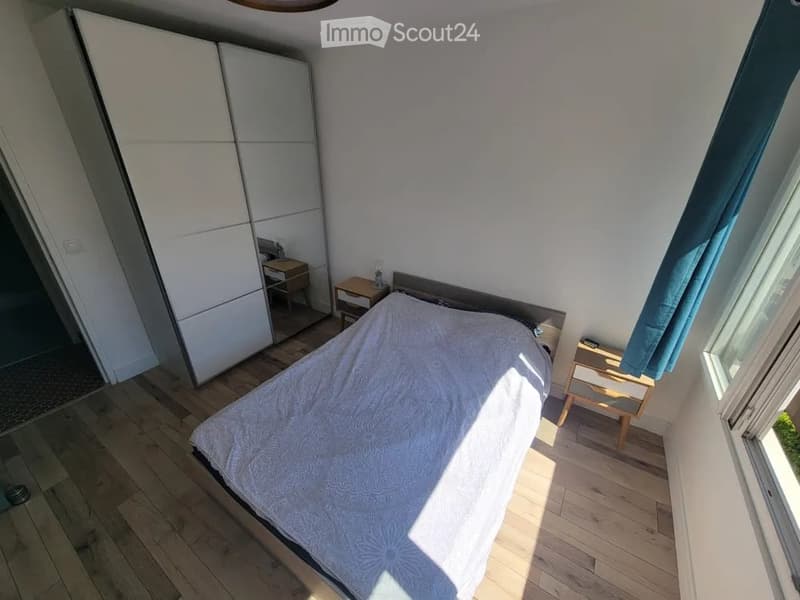 Bright bedroom with wooden flooring, a neatly made bed, two nightstands, a wardrobe, and a lamp on one nightstand.