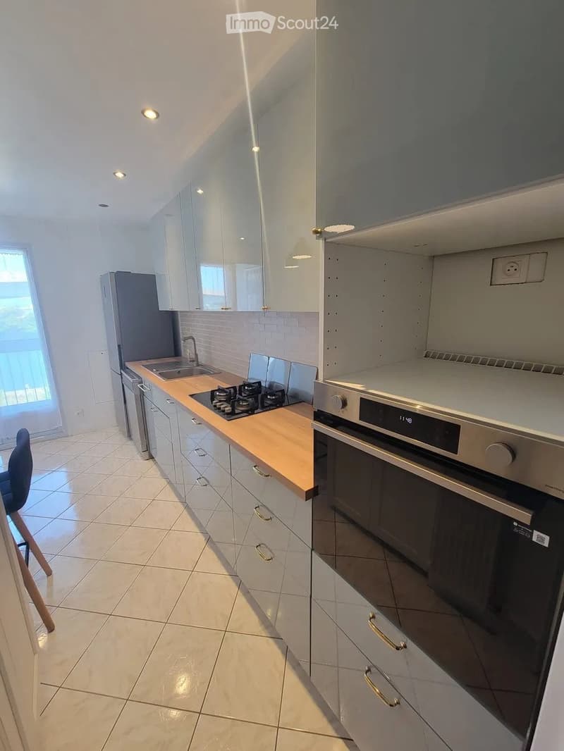 Modern kitchen with white cabinets, light wooden countertops, stainless steel appliances, and a gas stove. Features a sink, refrigerator, and a single chair near the window.
