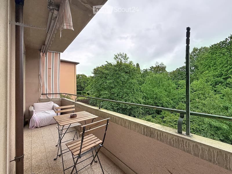 Balcony with a sofa, small table, and chairs, overlooking a lush green area.