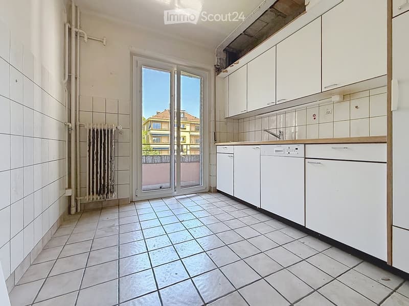Modern kitchen with white cabinets, a dishwasher, and a tiled floor. A large window offers a view of the outside.