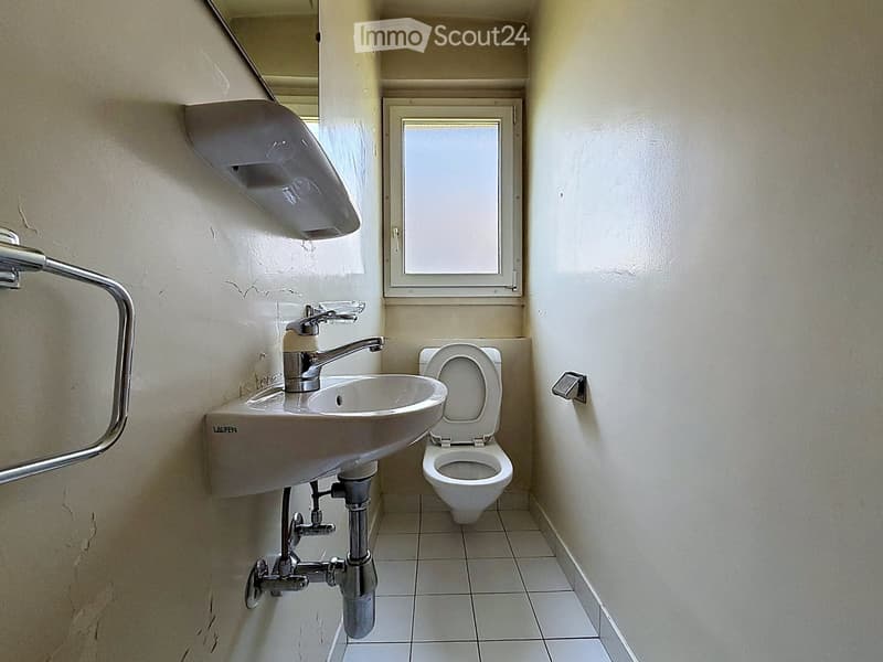 Small bathroom with a white sink, faucet, and toilet. The walls are light-colored with a small window above the toilet.