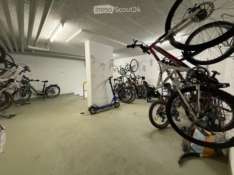 A storage area with multiple bicycles and a scooter, organized on racks and leaning against the walls.