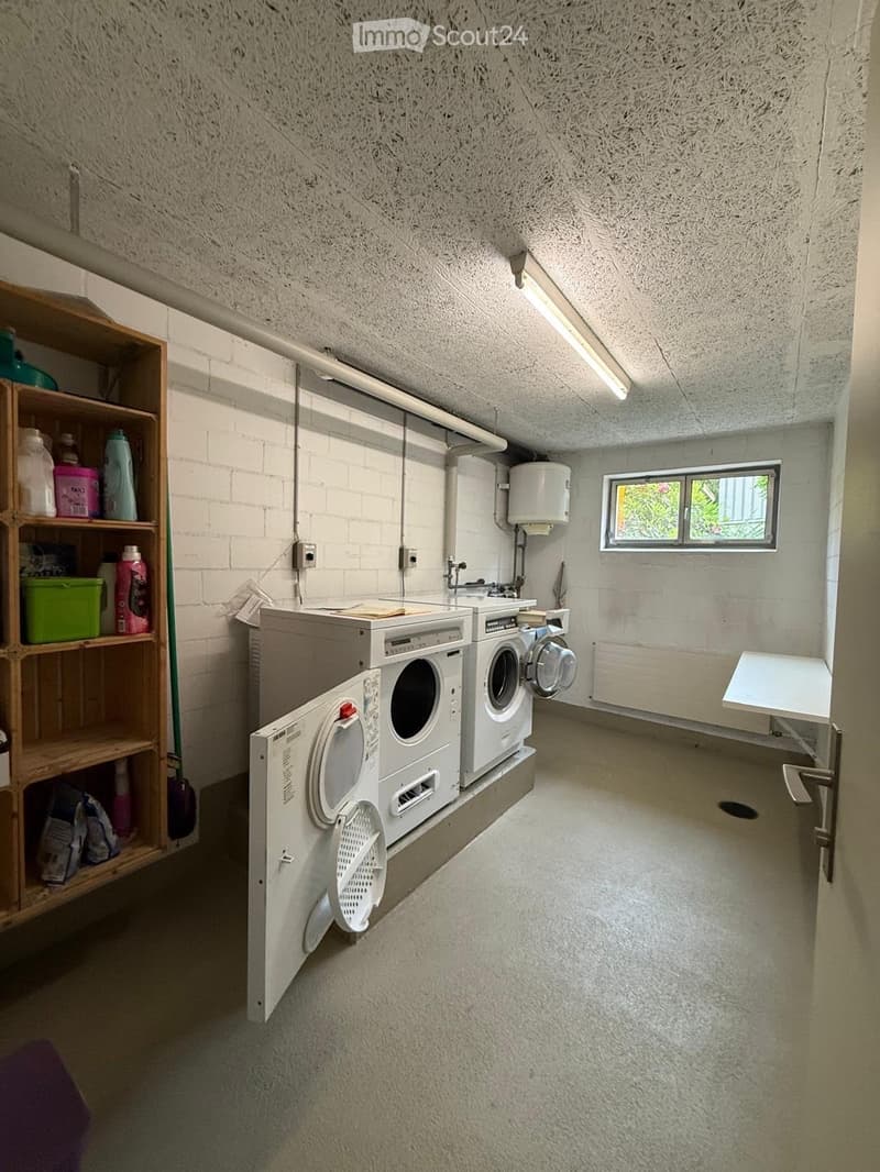 Laundry room with washing machine, dryer, wooden shelf, and small table.