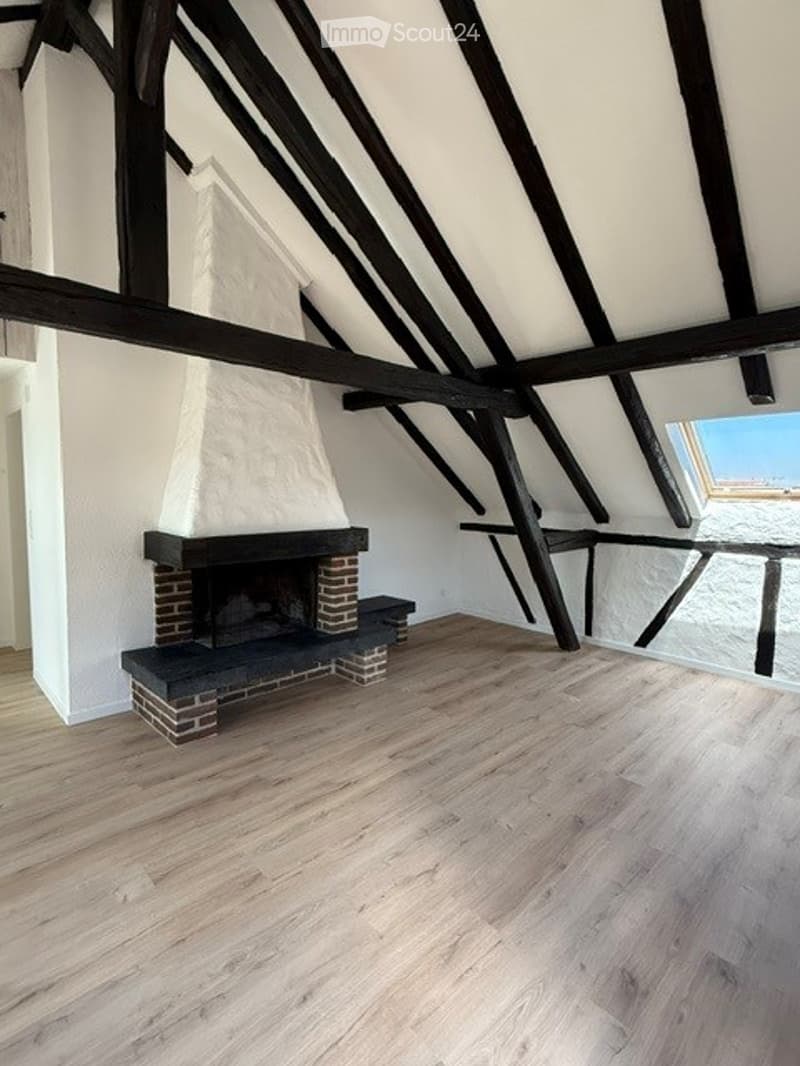 An unfurnished room with exposed wooden beams, a brick fireplace, and wooden flooring.