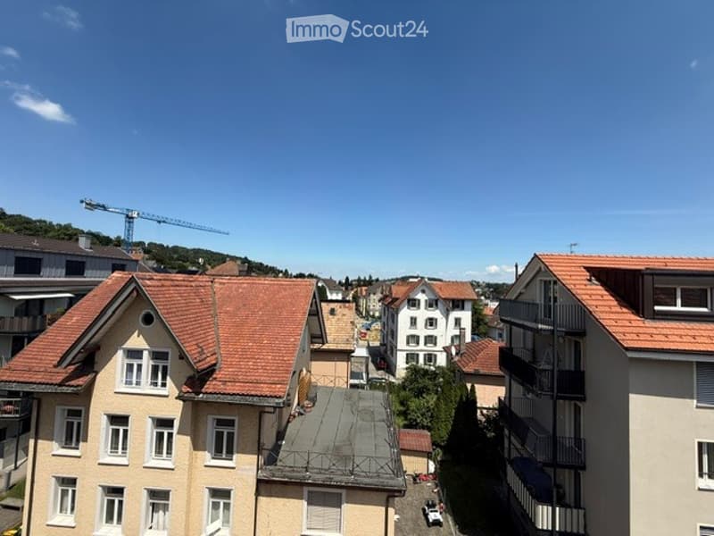 A view of a residential area with multiple buildings, including houses with red-tiled roofs and balconies, and a construction crane in the background.