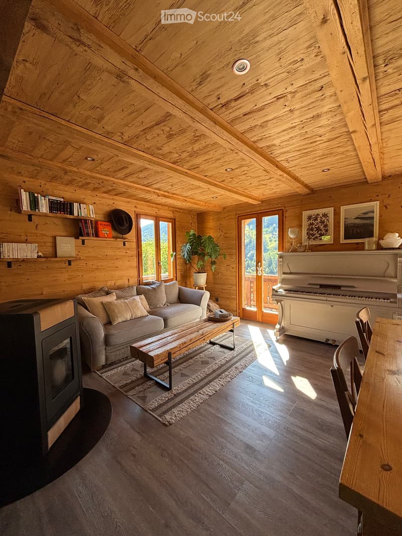 Cozy living room with wooden walls and ceiling, large windows offering a scenic view, a sofa, coffee table, piano, and fireplace.