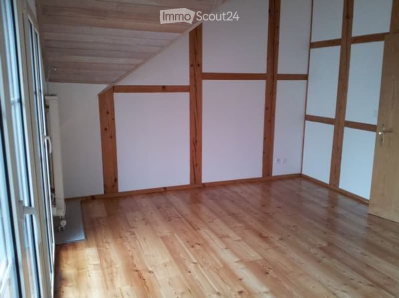 Completely empty room with wooden floor, white walls, and wooden beams on the ceiling. No furniture or equipment.