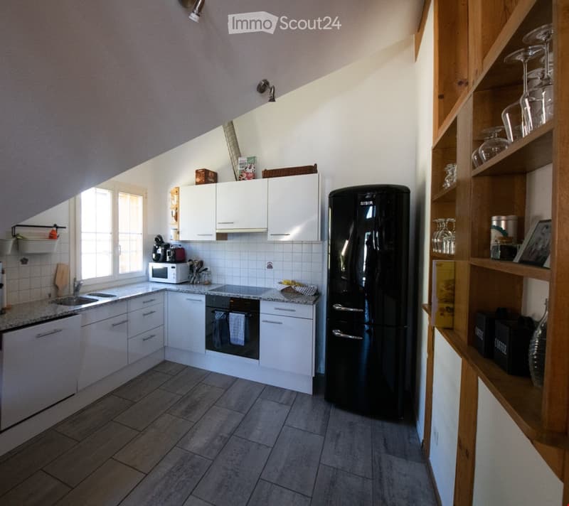 Modern kitchen with white cabinets, granite countertops, and a black refrigerator. Includes a microwave, oven, sink, and wooden shelves with glassware and decorative items.