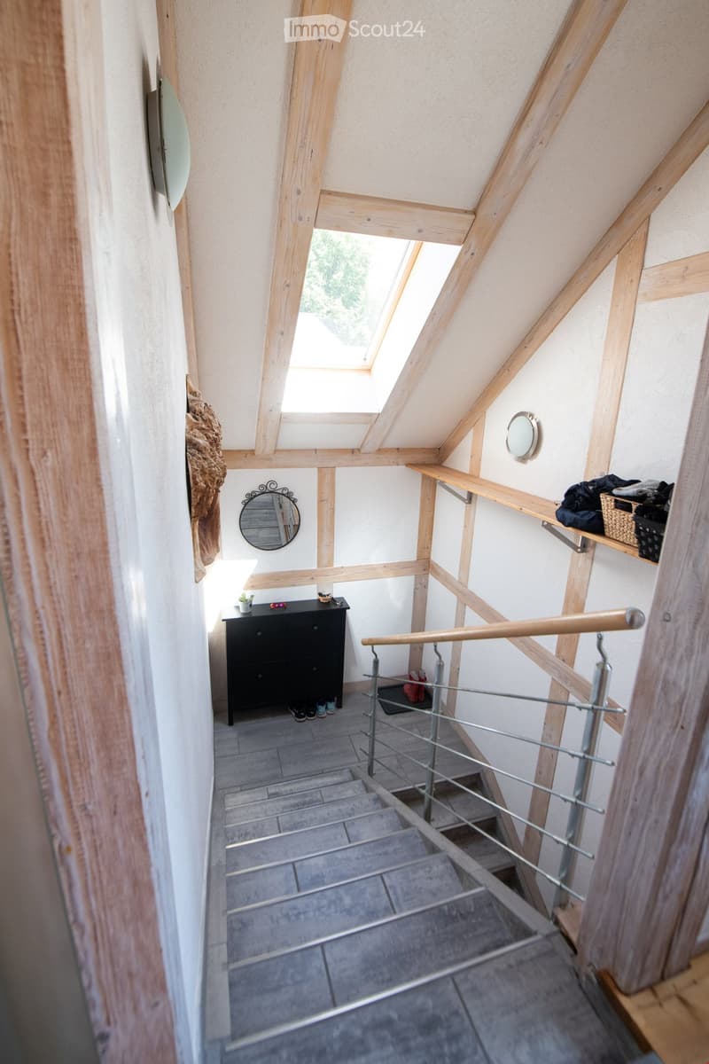Modern hallway with wooden beams, skylight, built-in shelving, small black cabinet, and decorative mirrors.