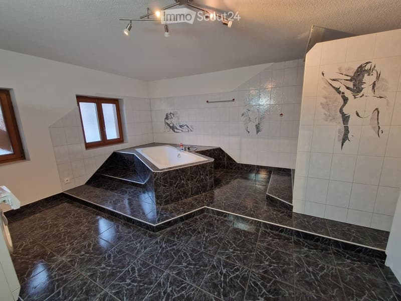 Modern bathroom with dark marble tiles, a bathtub, and decorative wall art. Features a window and recessed lighting.