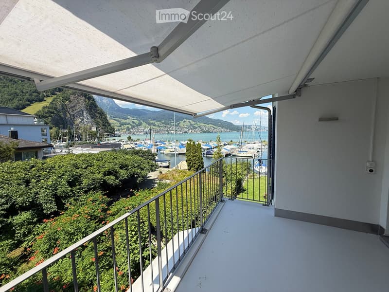 Balcony with retractable awning, metal railing, and scenic view of a lake, boats, and mountains.