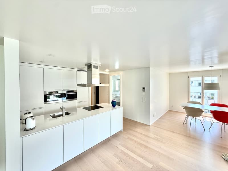 Modern kitchen with white cabinets, stainless steel appliances, island with sink and faucet, and a dining area with a table and chairs.