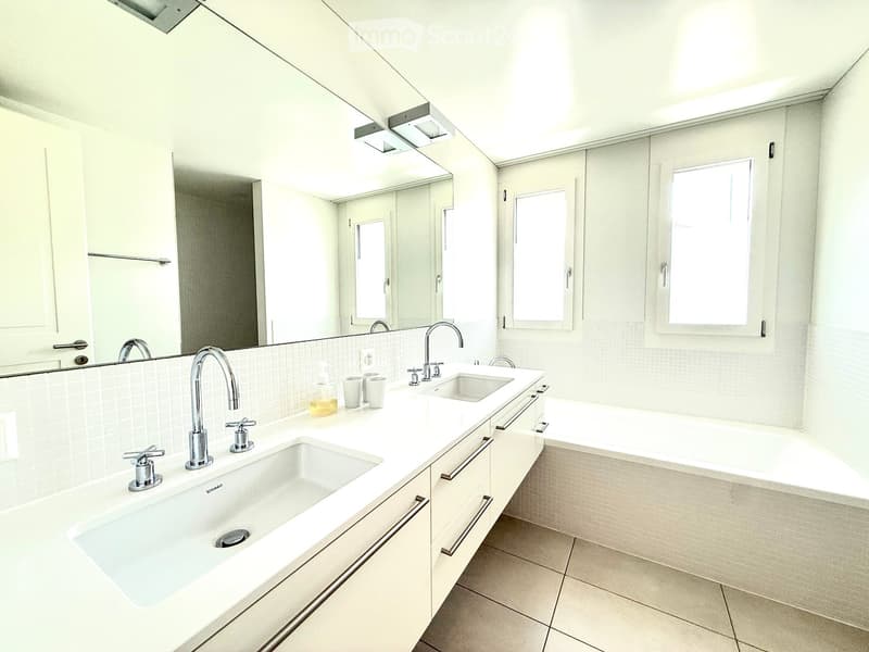 Modern bathroom with double sink, bathtub, large mirror, and natural light from windows.