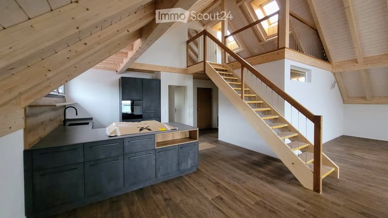 Modern kitchen with wooden floors, grey cabinets, a central island, and a staircase leading to an upper level.