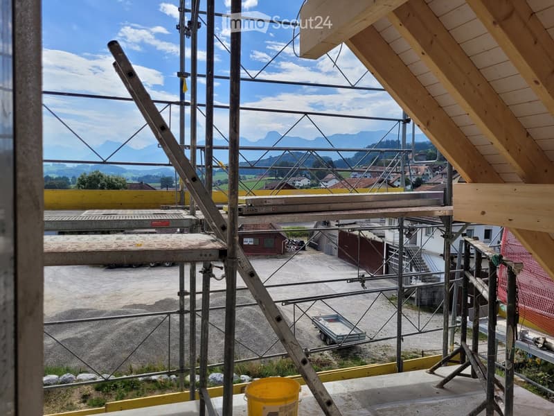 View from a rooftop under construction, showing scaffolding, wooden beams, and a distant landscape with mountains and houses.