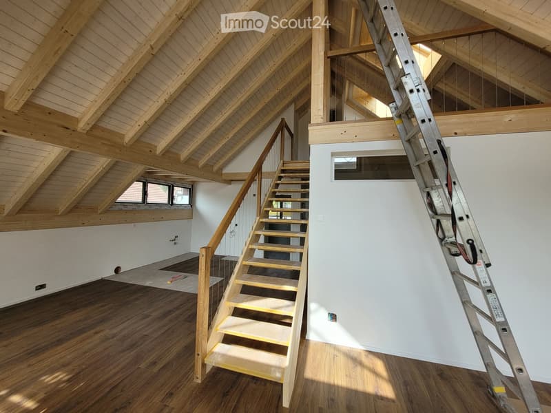 Open, unfinished attic space with exposed wooden beams, wooden staircase leading to a loft area, and a ladder leaning against the wall.