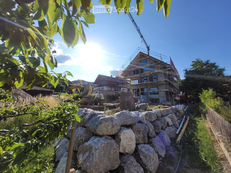 A multi-story house under construction with scaffolding, surrounded by greenery and construction materials.