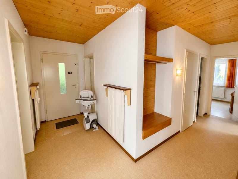Hallway with wooden ceiling, white walls, carpeted floor, radiator, shelf, and exercise bike in the corner.