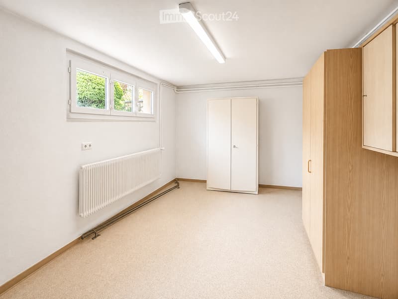 Empty room with white walls, carpeted floor, large window, radiator, built-in closet, and wooden wardrobe.