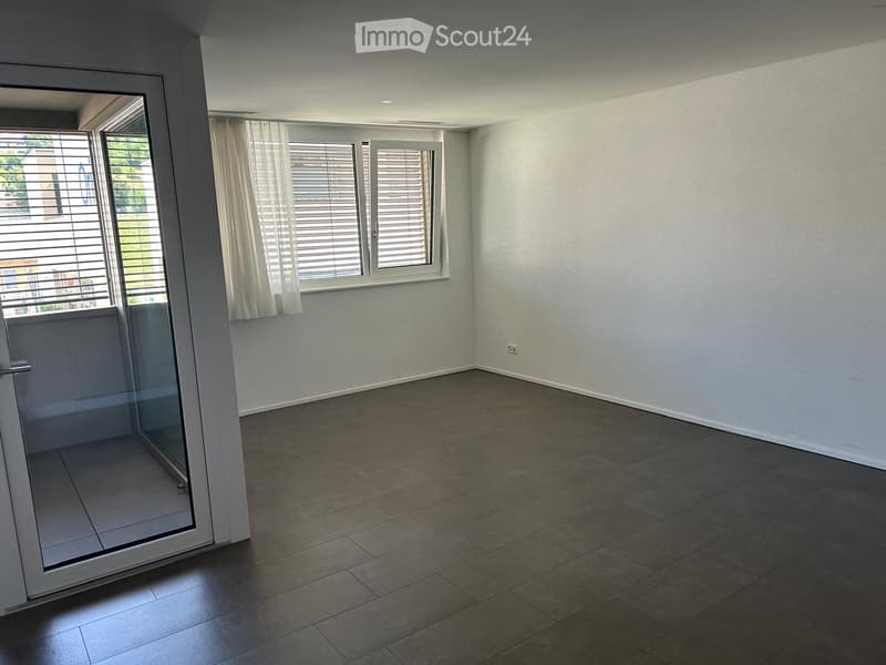 Empty room with tiled floor, white walls, large windows with blinds, and a sliding glass door leading to a balcony.
