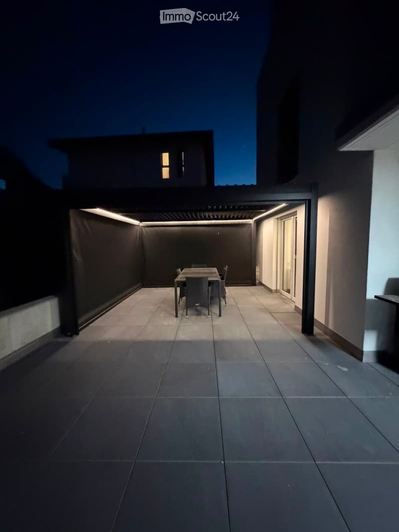 Modern outdoor dining area with a table and chairs, surrounded by sleek walls and illuminated by ambient lighting.