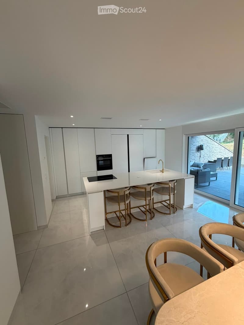 Modern kitchen with white cabinets, a central island with a built-in stove and sink, and beige chairs around a dining table.
