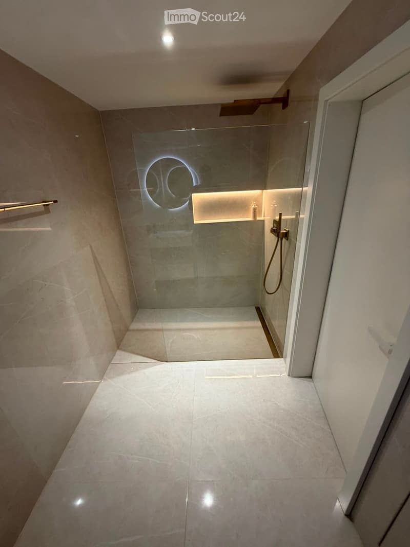 Modern bathroom with a glass-enclosed shower stall, sleek light fixtures, and a clean, minimalist design.