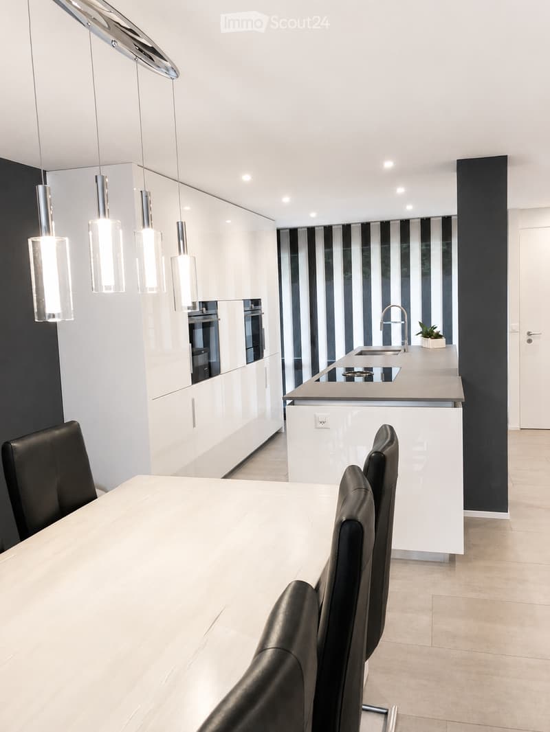 Modern kitchen and dining area with white cabinets, a central island, pendant lights, and a dining table with black chairs.