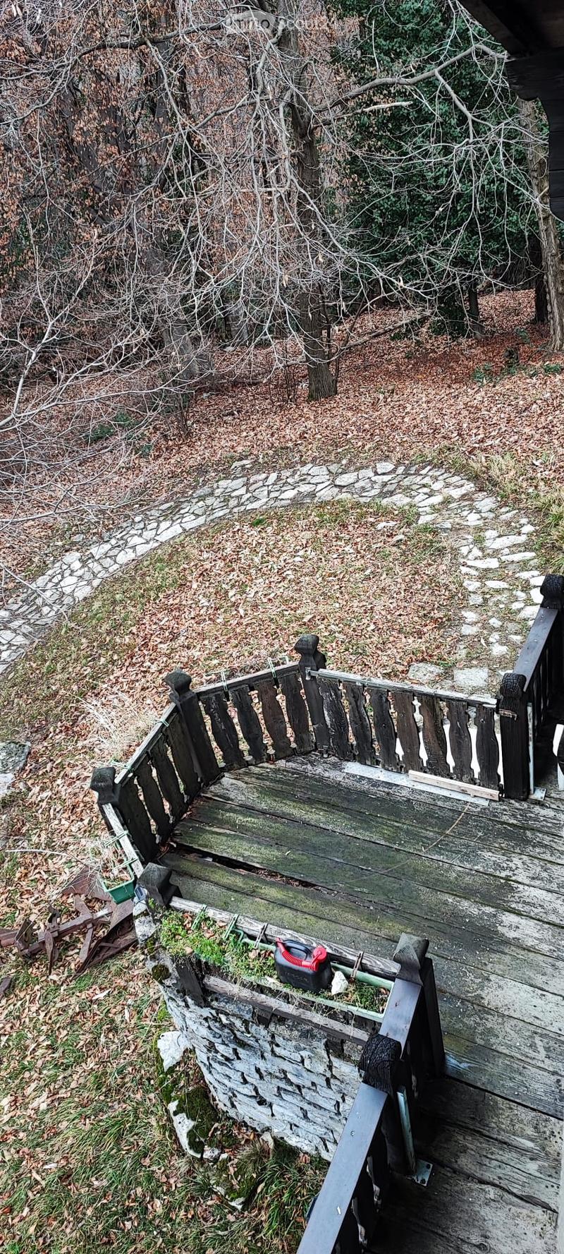 Wooden deck with railing, stone steps, scattered leaves, and a small container on the ground.