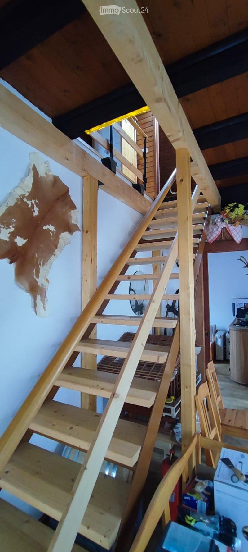 Wooden staircase leading to an upper level, with exposed wooden beams and a partially finished wall featuring a piece of animal hide.