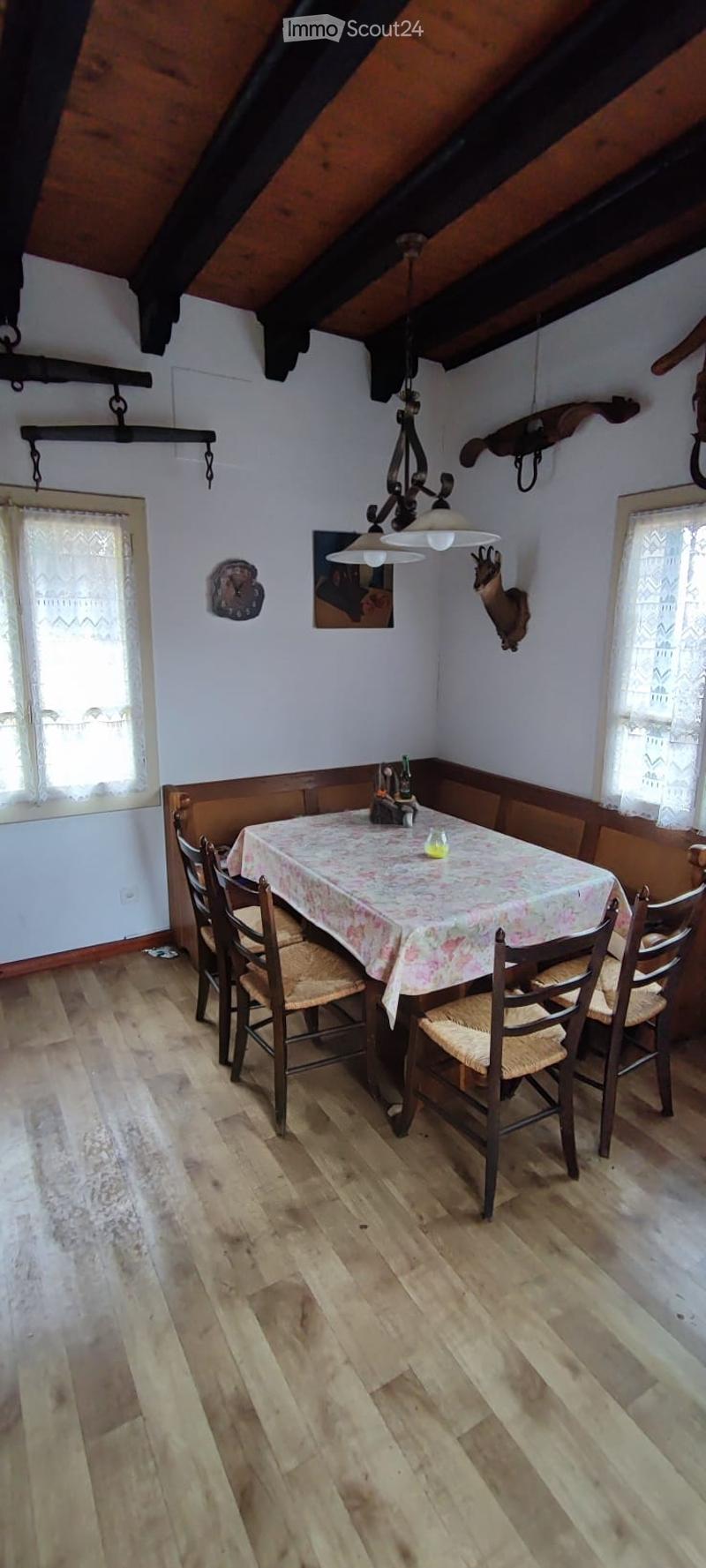 Dining area with wooden floor, chandelier, table with floral tablecloth, and chairs.