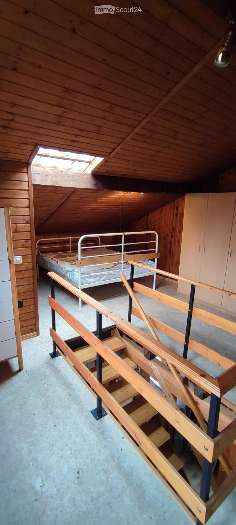 Loft-style bedroom with wooden walls, exposed wooden beams, a single bed with a metal frame, and built-in wooden cabinets.