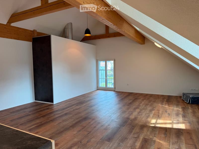 Empty attic room with wooden floors, white walls, exposed wooden beams, and a skylight window. No furniture or equipment present.