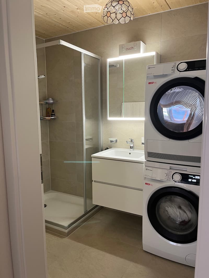 Modern bathroom with a sink, mirror, shower, and a stacked washing machine/dryer unit.